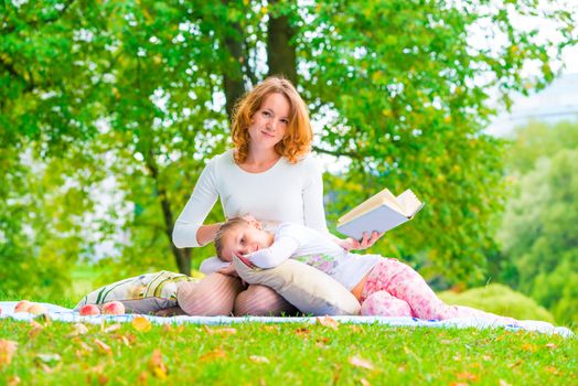 Beautiful mother and daughter resting in a park reading a book