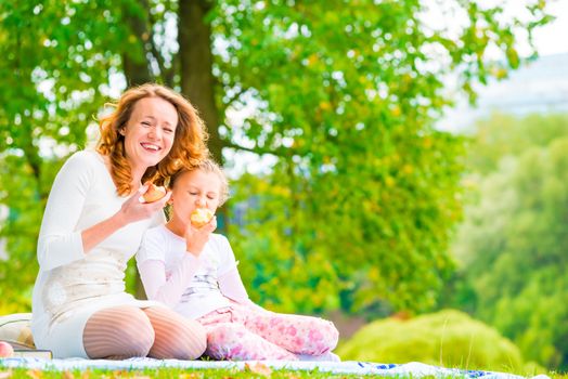 young mother and her daughter eating apples in the park