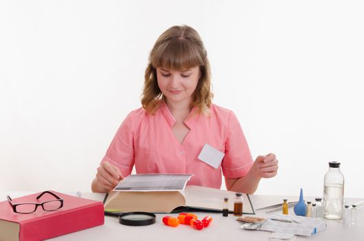 Pharmacist sitting at the table reading a thick handbook of medicines