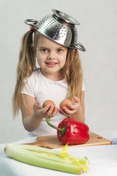 Girl playing in a cook. Carried away by the game she put on a colander on his head. In the hands of the girls two eggs. Studio. Light background.