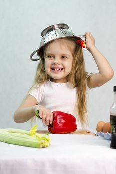 Girl playing in a cook. Carried away by the game she put on a colander on his head. Studio. Light background.