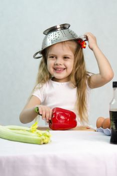 Girl playing in a cook. Carried away by the game she put on a colander on his head. Studio. Light background.