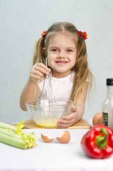 Girl playing in a cook. Girl churn whisk the eggs in a glass bowl. At the forefront of the shell, celery, pepper. Studio. Light background.
