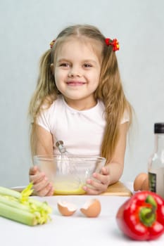 Girl playing in a cook. Girl churn whisk the eggs in a glass bowl. At the forefront of the shell, celery, pepper. Studio. Light background.