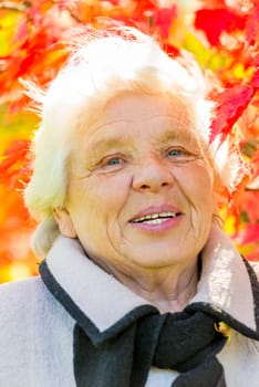 Vertical portrait of an elderly woman on a background of red leaves