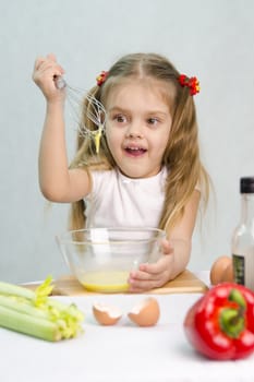 Girl playing in a cook. Girl churn whisk the eggs in a glass bowl. At the forefront of the shell, celery, pepper. Studio. Light background.