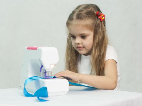 Girl sew on a children's sewing machine. Studio, a white background.