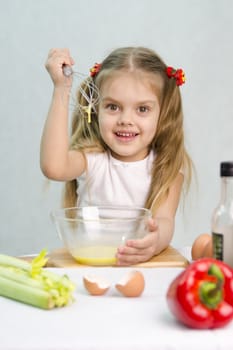 Girl playing in a cook. Girl churn whisk the eggs in a glass bowl. At the forefront of the shell, celery, pepper. Studio. Light background.