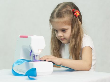 Girl sew on a children's sewing machine. Studio, a white background.