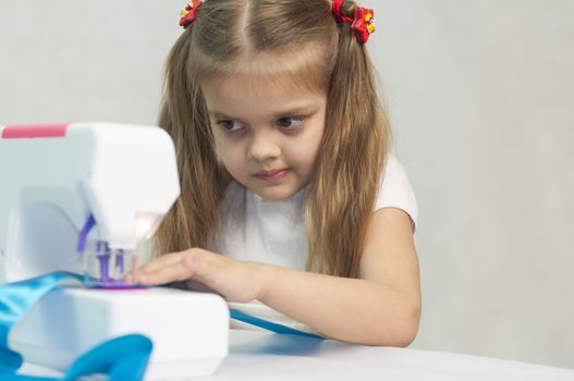 Girl sew on a children's sewing machine. Studio, a white background.