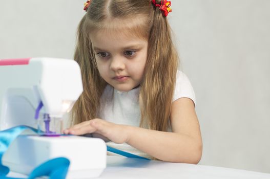 Girl sew on a children's sewing machine. Studio, a white background.