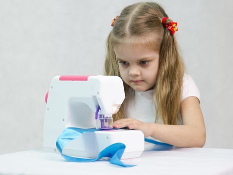 Girl sew on a children's sewing machine. Studio, a white background.