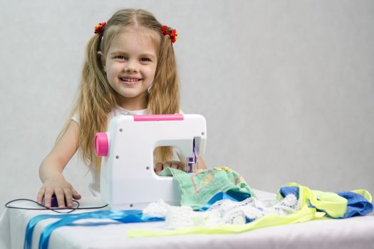 Girl sew on a children's sewing machine. Studio, a white background.