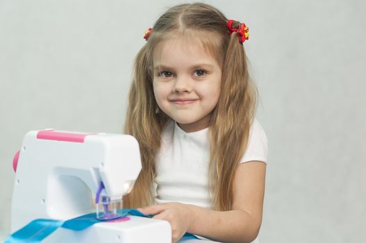 Girl sew on a children's sewing machine. Studio, a white background.