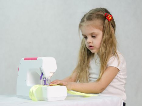 Girl sew on a children's sewing machine. Studio, a white background.