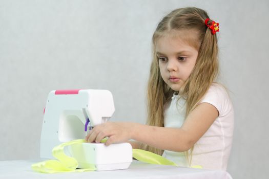 Girl sew on a children's sewing machine. Studio, a white background.
