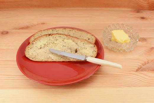 Buttered slices of bread on a red plate with a knife and butter dish