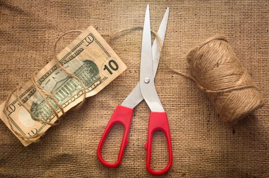 A scissor cutting a rope holding a 10 dollar bill