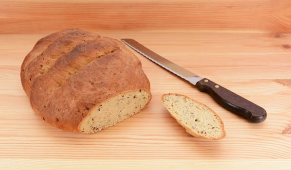 Freshly baked loaf of bread with the first slice taken and a bread knife on the table