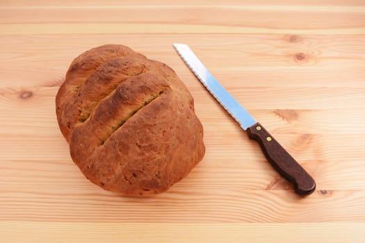 Freshly baked seeded loaf with a bread knife on a wooden table 