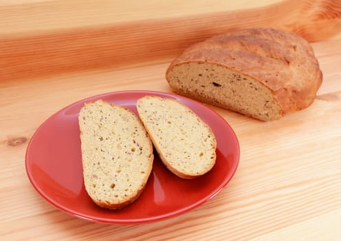 Two slices of bread on a red plate, with a seeded loaf of bread on a wooden table