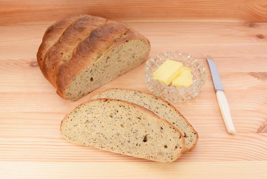 Fresh bread - loaf and slices - with a butter dish and knife on a wooden table