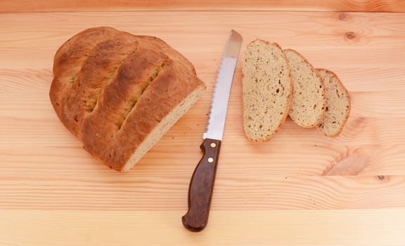 Fresh loaf of bread with a sharp knife and three cut slices on a pine table