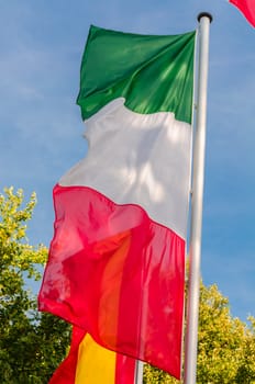 Italian flag on a flag pole waving in the wind against blue sky