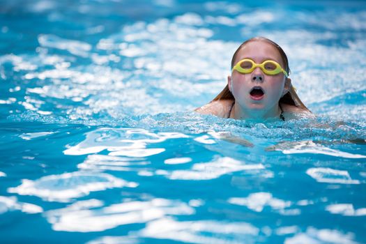 Young girl in goggles and cap swimming breast stroke style in the blue water pool