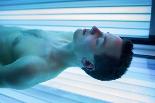 Handsome young man relaxing during a tanning session in a modern solarium, taking care of himself, enjoying the artificial sunlight.