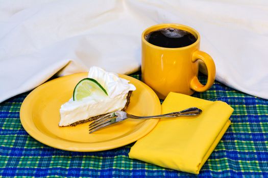 Slice of key lime pie with coffee on plate with fork and napkin.