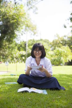 Girl sitting homework and reading. On the grass in the park.