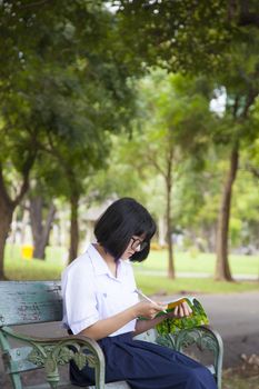 Girl sitting and reading a book. Sit on a bench in the park.