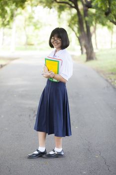 Schoolgirl standing holding a book. Relaxed, smiling and happy. In the park