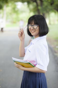 Schoolgirl standing holding a book. Relaxed, smiling and happy. In the park