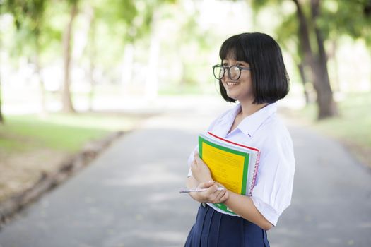 Schoolgirl standing holding a book. Relaxed, smiling and happy. In the park