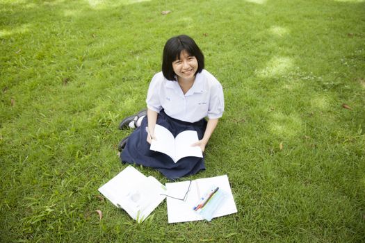 Schoolgirl was reading and homework on the grass in the park a happy.