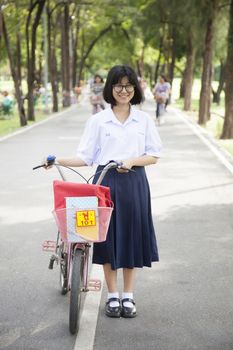 Schoolgirl. Standing and holding bike on the road. Within the park. Smiling and happy
