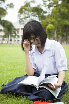 Schoolgirl was reading on the grass in the park seriously.