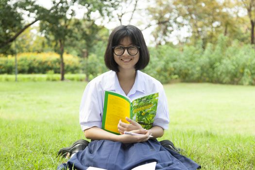 Girl holding a book and smiling. Sitting on the grass in the garden.