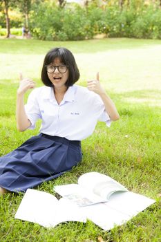Schoolgirl smiling and sitting homework. On grass in park.
