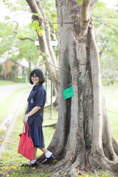 Girl wearing glasses a red holding the bag. Smiling a happy Standing under a tree in the park.