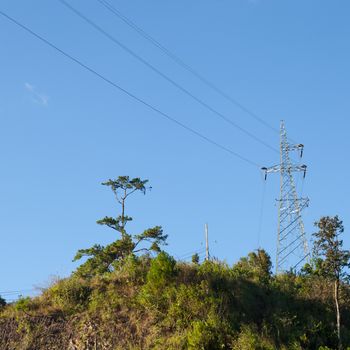 High voltage pylons. On a mountain with trees. Cloudy and clear sky.