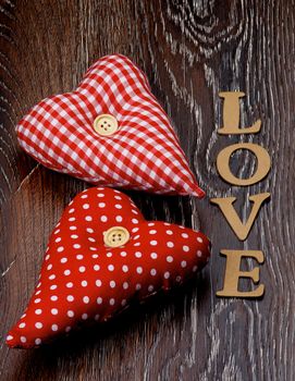 Arrangement of Two Handmade Textile Red Polka Dot Hearts and Cardboard Word Love closeup on Dark Wooden background