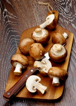 Arrangement of Gourmet Raw Portabello Mushrooms with Table Knife on Cutting Board closeup on Dark Wooden background