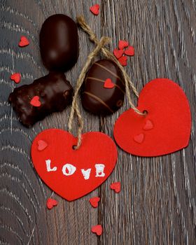 Two Red Hearts with Word Love, Chocolate Candies and Small Hearts closeup on Dark Wooden background