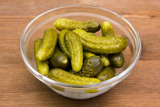 Pickled cucumbers on glass bowl on wooden table