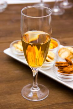 Flute with aperitif and pretzels on wooden table seen close