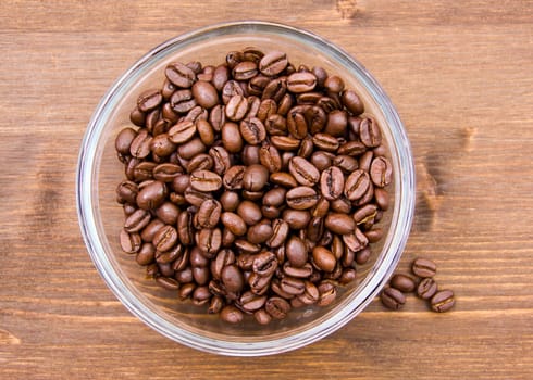 Coffee beans on bowl on wooden table seen from above