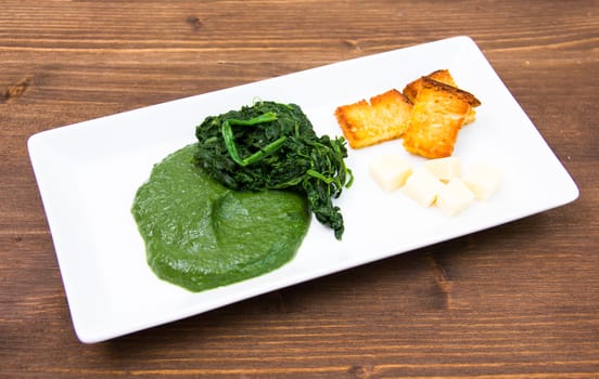 Tray with creamed spinach and croutons on wooden table